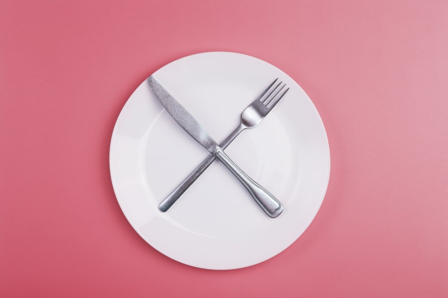 Empty plate on a pink minimal background. Empty white ceramic plate with knife and fork on the table after eating.