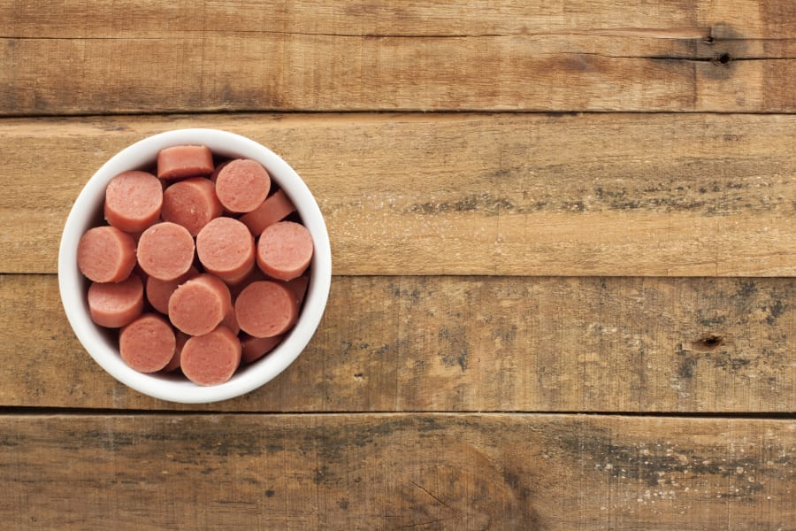 Top view of white bowl full of chopped sausages over wooden table