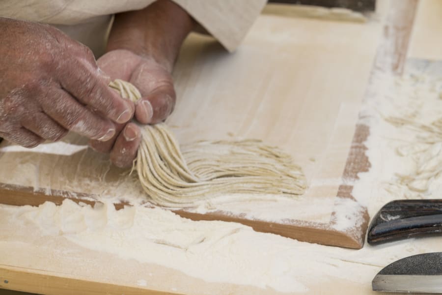 Making of fresh soba noodles, male hand with kitchen holding fresh bunch of noodles in hand on wooden desk.