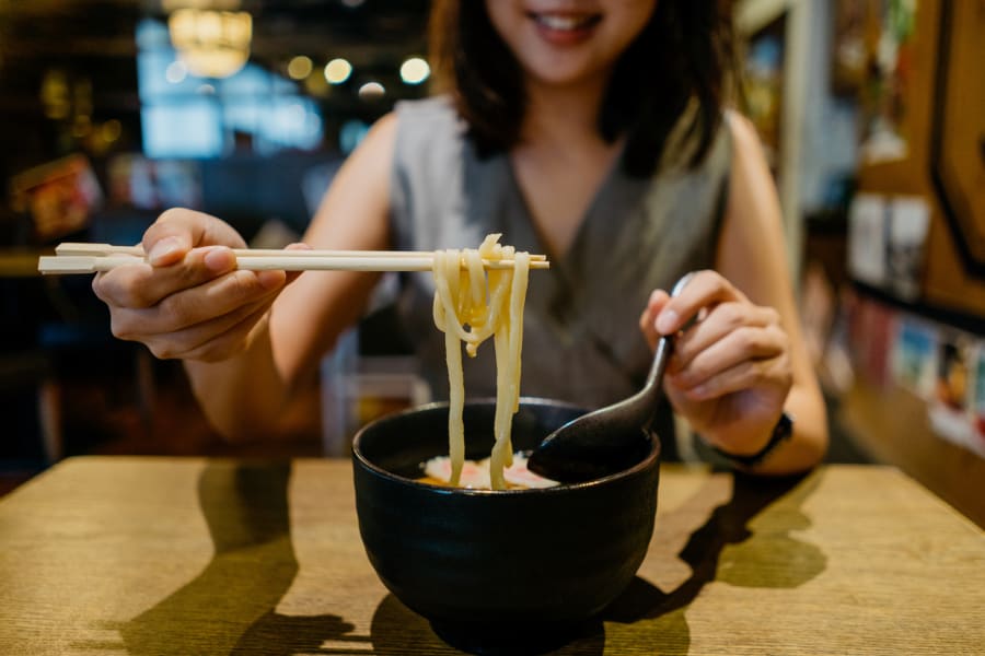 Young asian woman enjoying a bowl of Japanese Kitsune Udon in restaurant