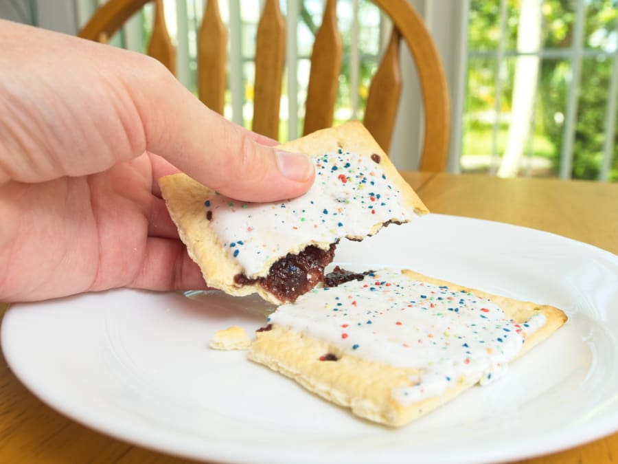 A sweet toaster pastry treat being split open with a human hand on a white plate.