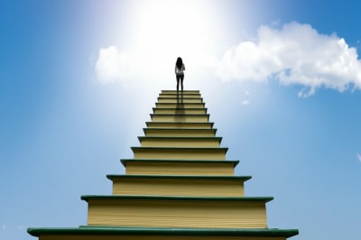 A person climbing a staircase made of books, reaching for a bright sky, symbolizing English language learning success.
