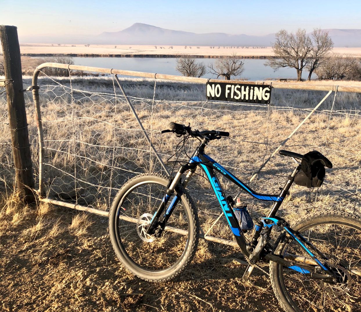 bicycle resting agaisnt country-side gate with a no fishing sign