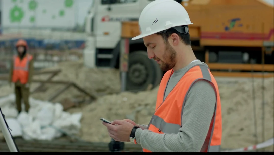 Alt=”Obrero en obra consultando el móvil durante su jornada laboral”