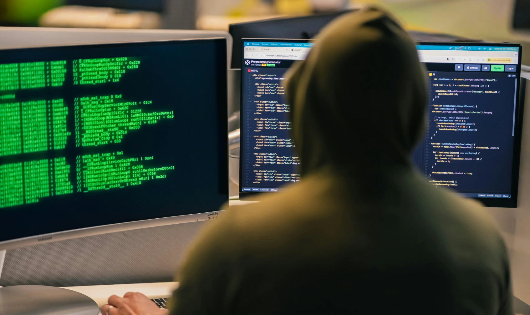 ciberataque: hacker con capucha frente a varias pantallas en oficina oscura, foto conceptual