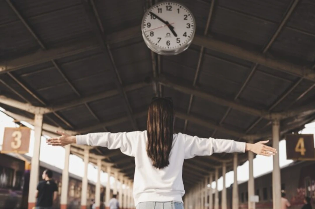 Entra 10 minutos antes: persona de espaldas bajo un reloj de estación, símbolo de llegar antes al trabajo.