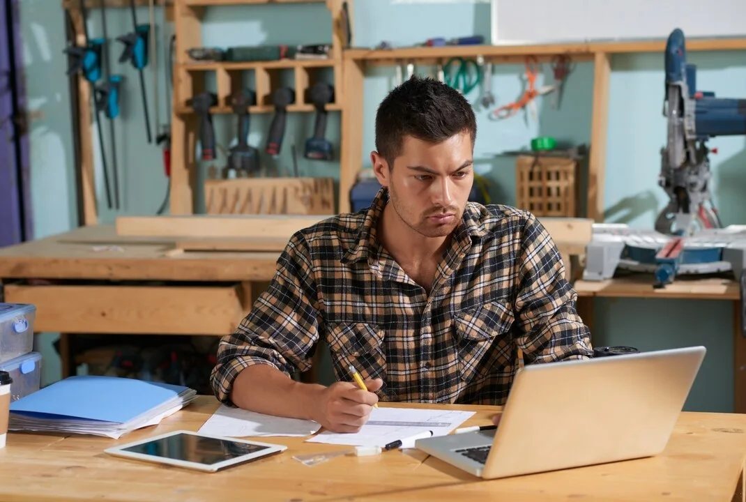 Trabajador en taller revisando documentos de la declaración de la renta 2025 con ordenador portátil