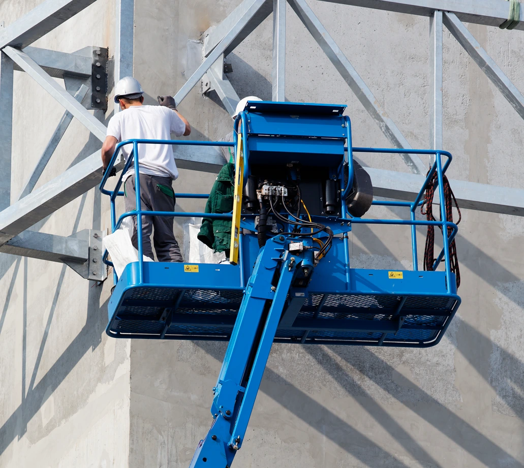 Dos trabajadores de construcción en plataforma elevadora realizando trabajos en altura sobre estructura de hormigón