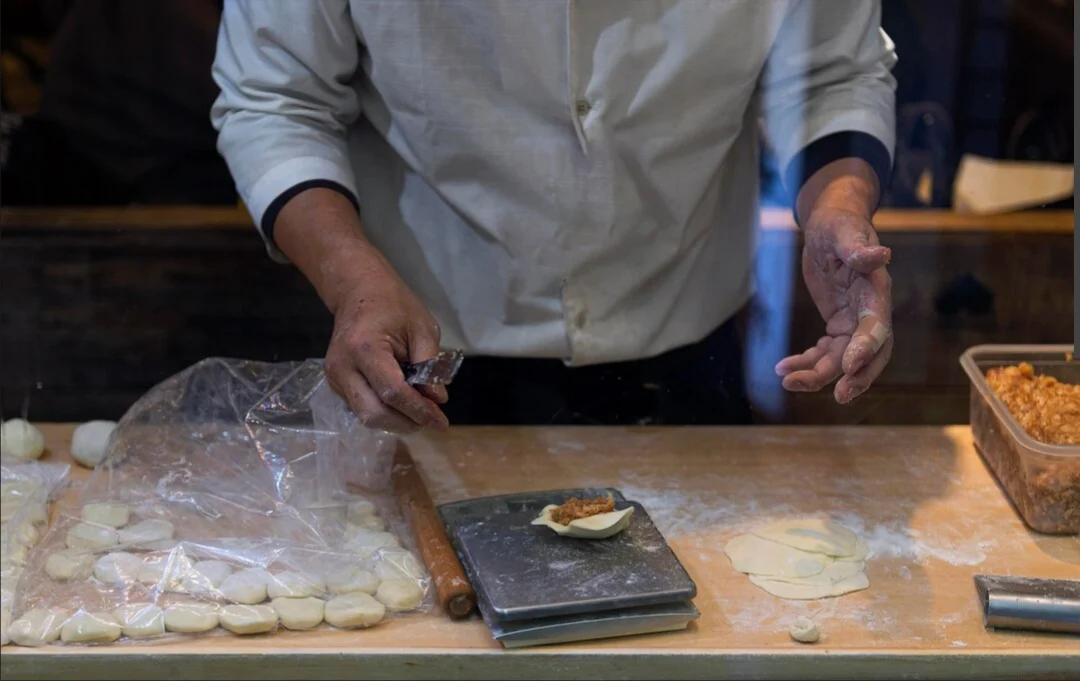 Trabajador manipulando alimentos en cocina industrial, manos enharinadas sobre mesa de trabajo
