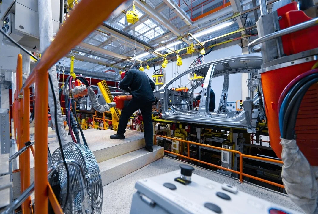 Operario de espaldas trabajando sobre la carrocería de un vehículo en una cadena de montaje de una planta de fabricación de automóviles.