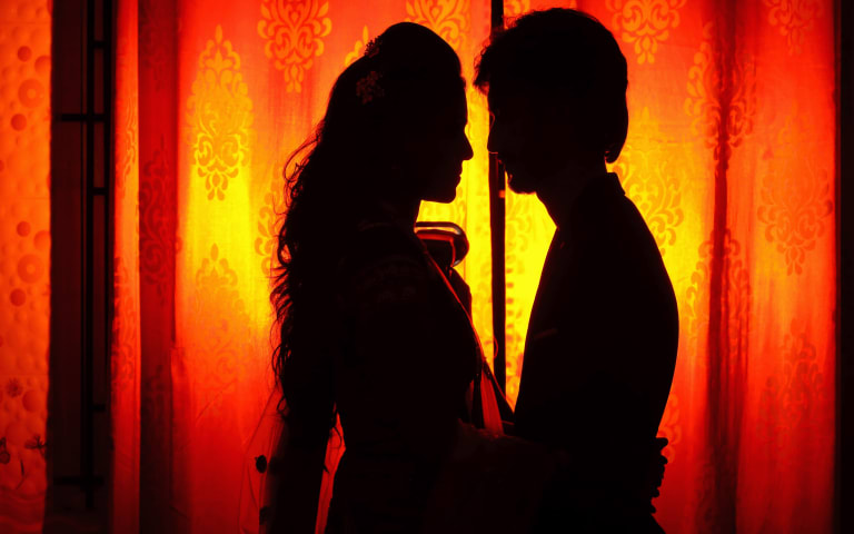 Silhouette of two lovers facing each other against a vibrant orange background.