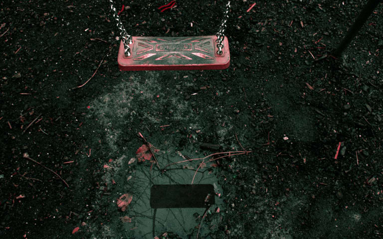 Empty red swing seat over wet ground.
