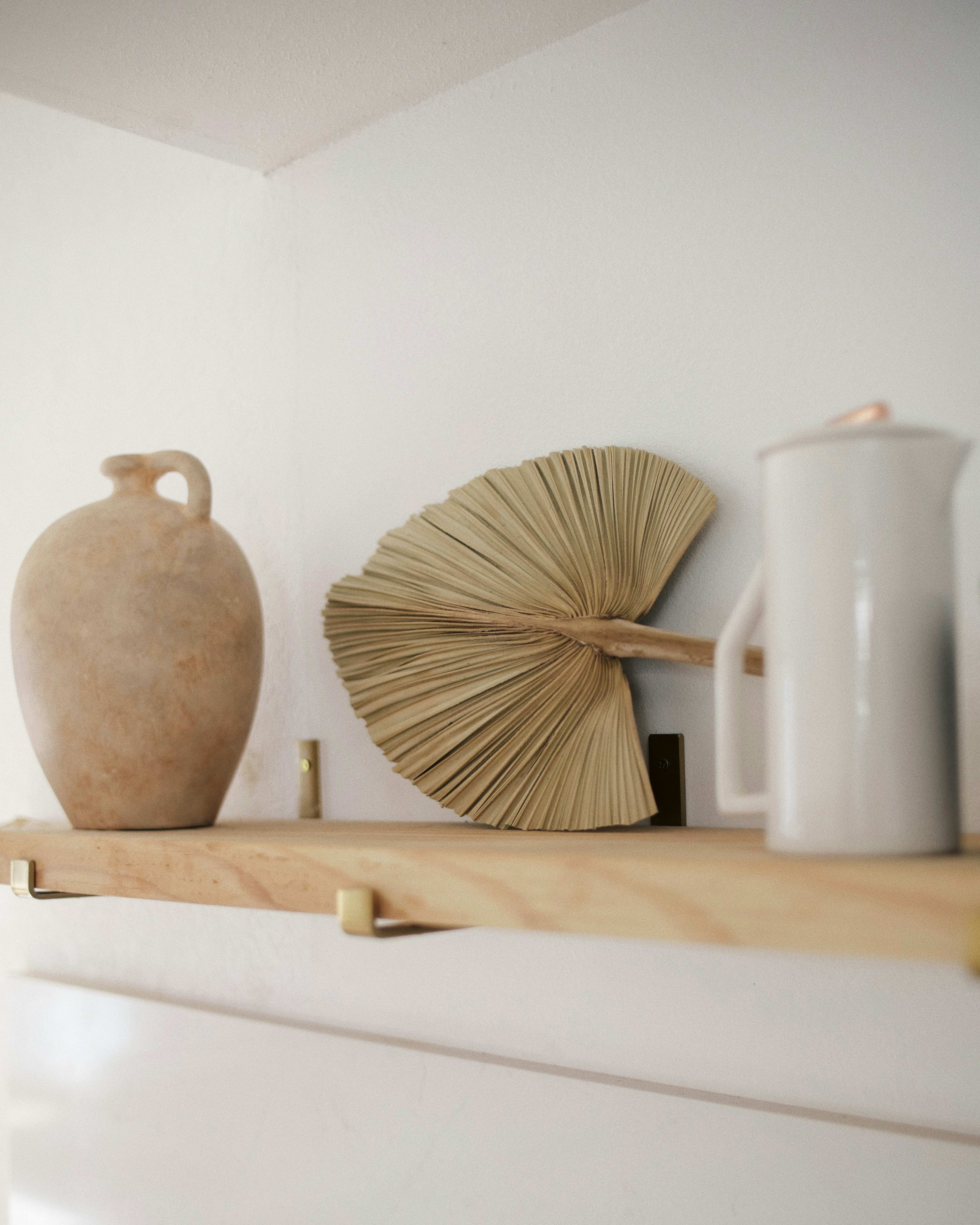 Clay vase and a dried palm leaf on a shelf