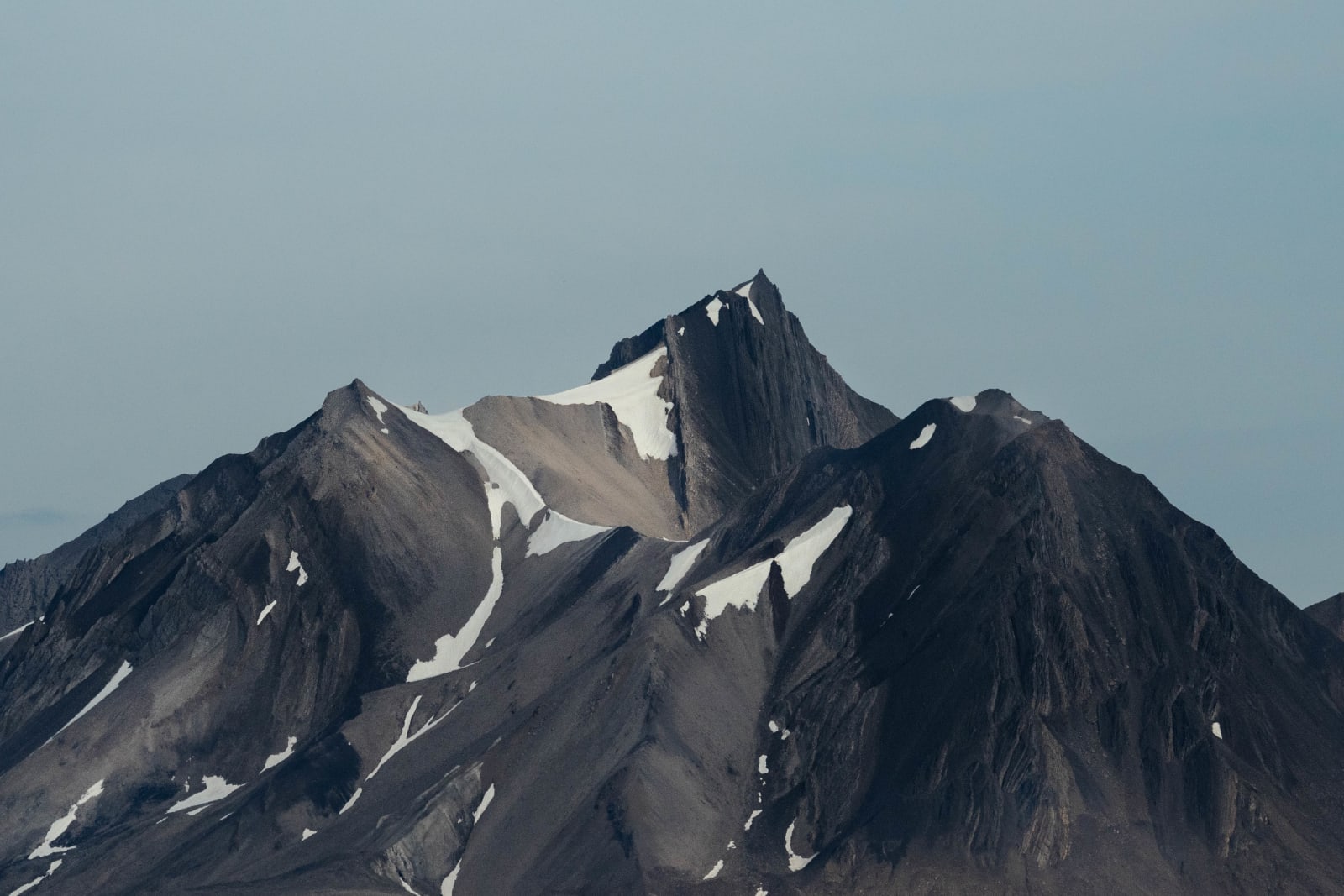 Very pointy mountains, on a sunny day. Both the mountains and the sky have a bright light blue/aqua color tone, and there are some patches of snow on the mountains.