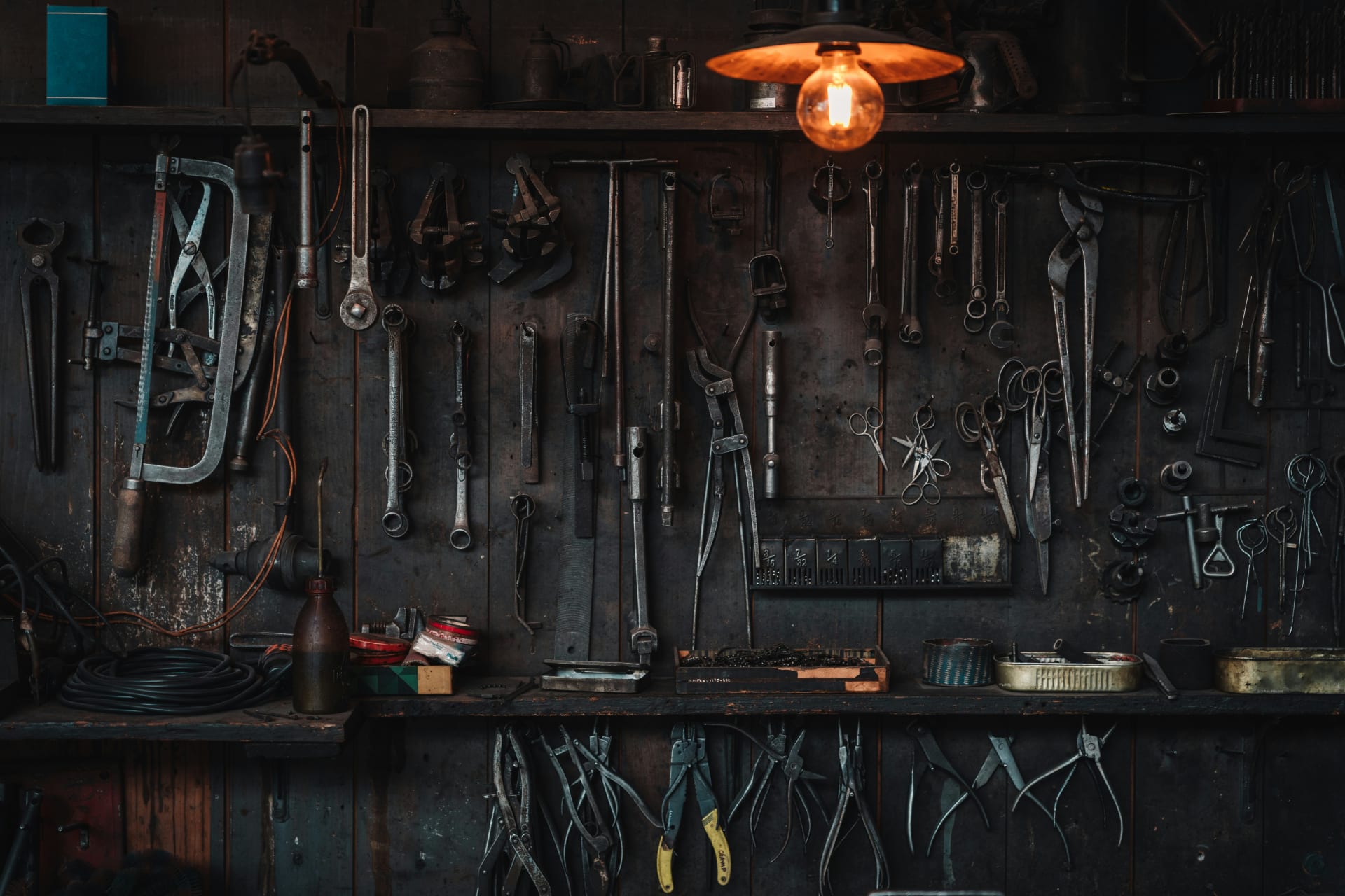 A wall of worn hand tools under a single lamp.