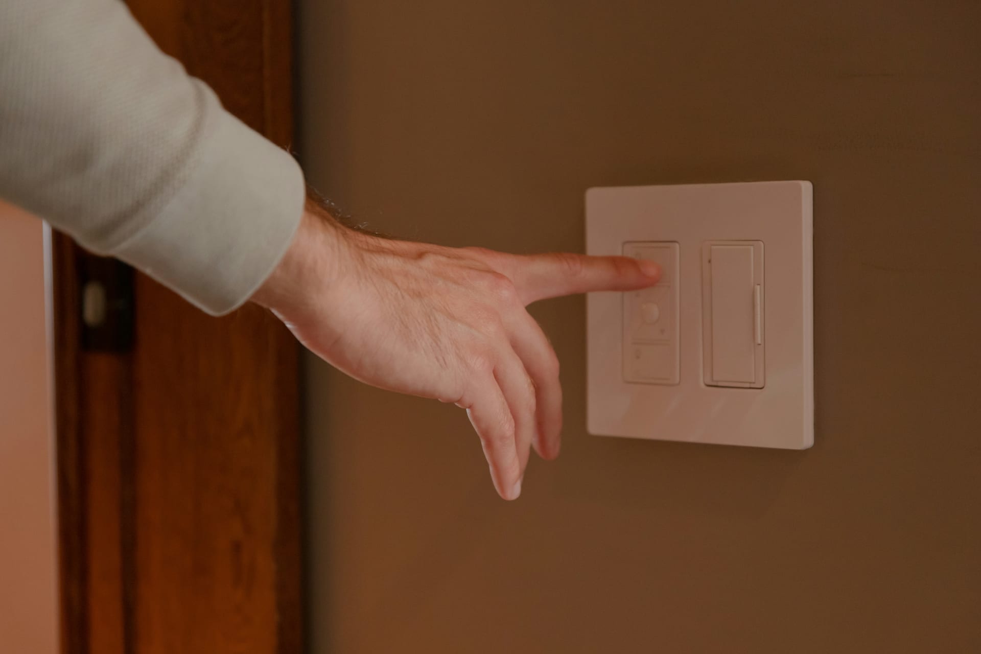 A hand reaching for a light switch on a dark wall.
