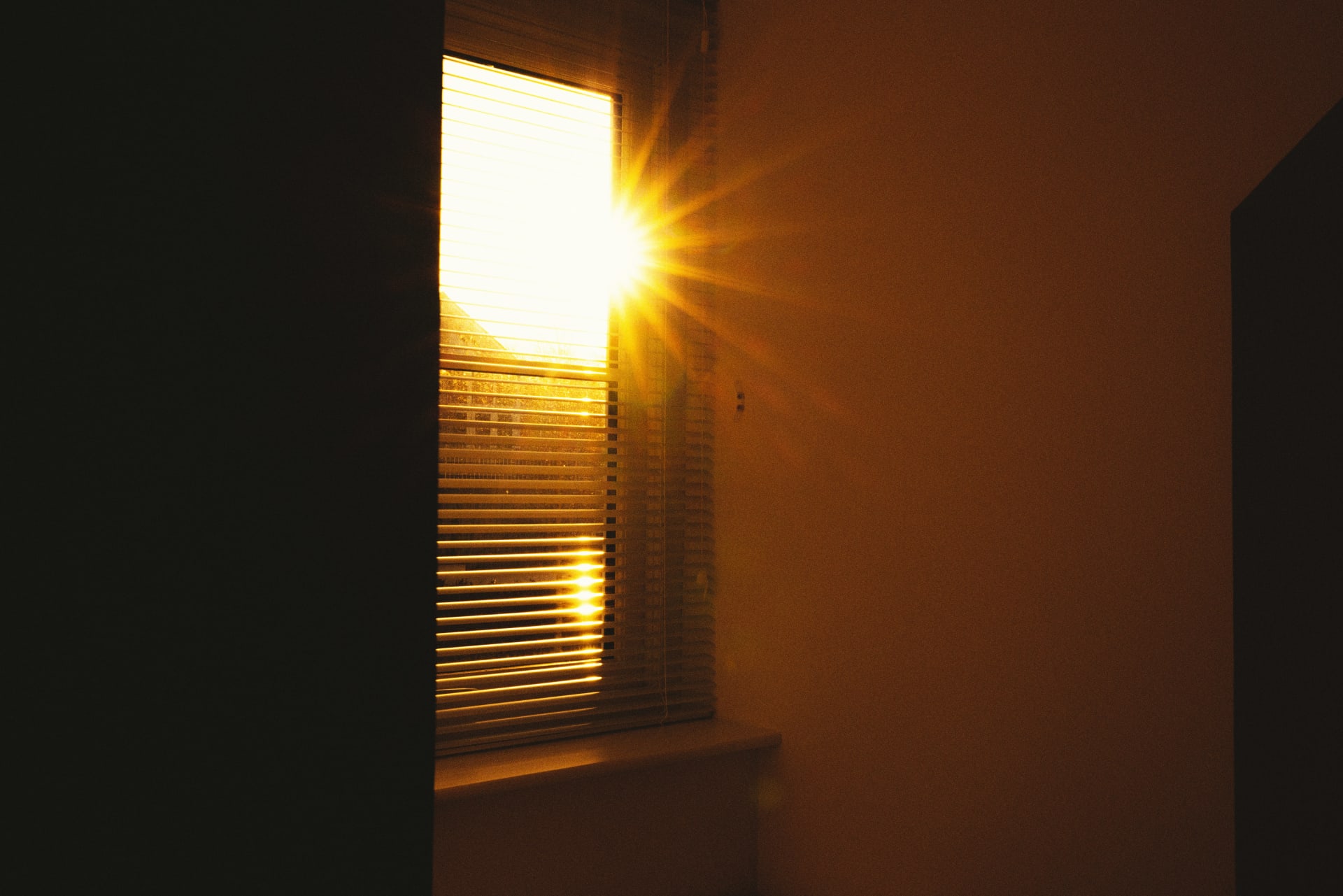 Low sun through a window blind into a dark room.