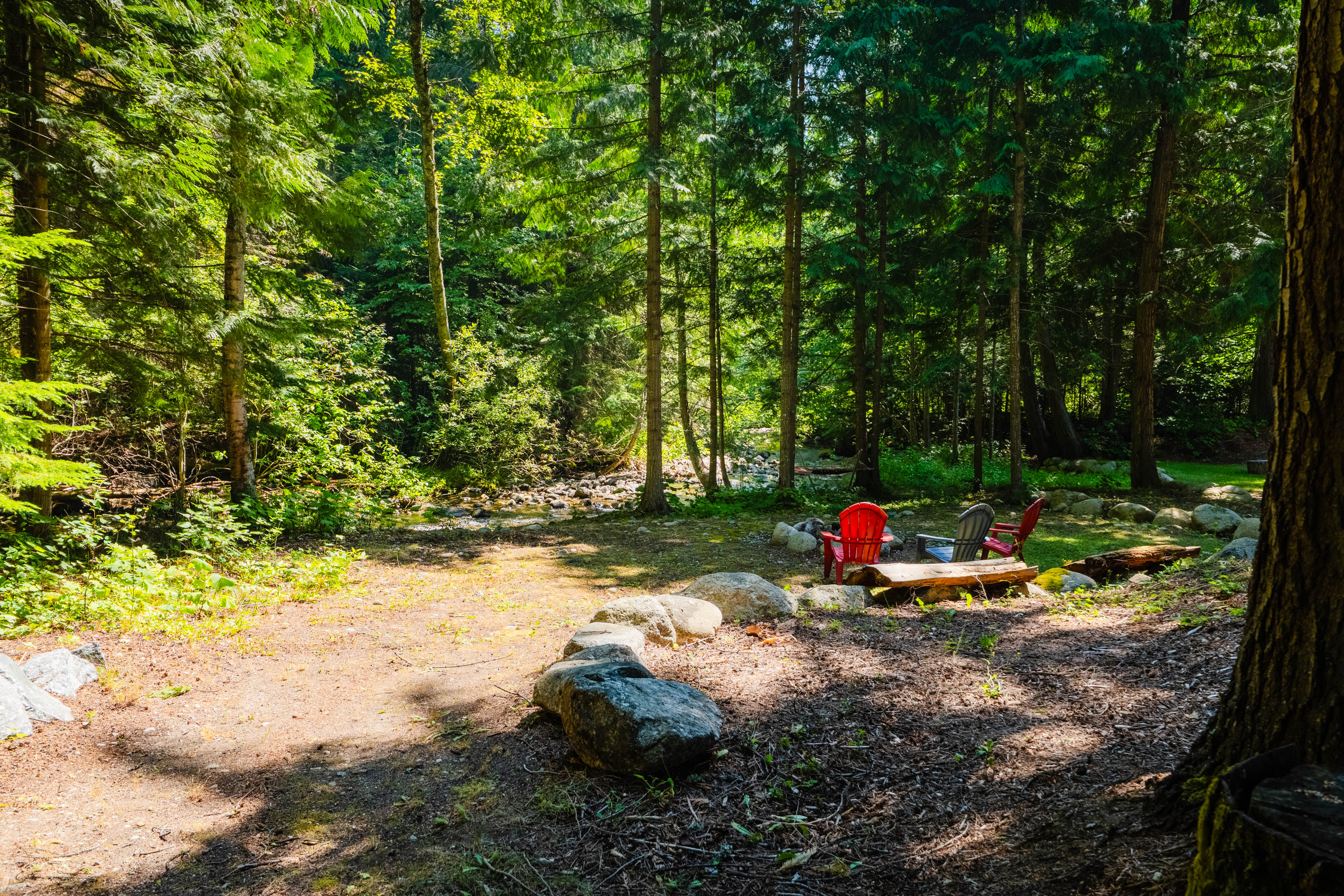 Red chairs tucked into the creekside woodland