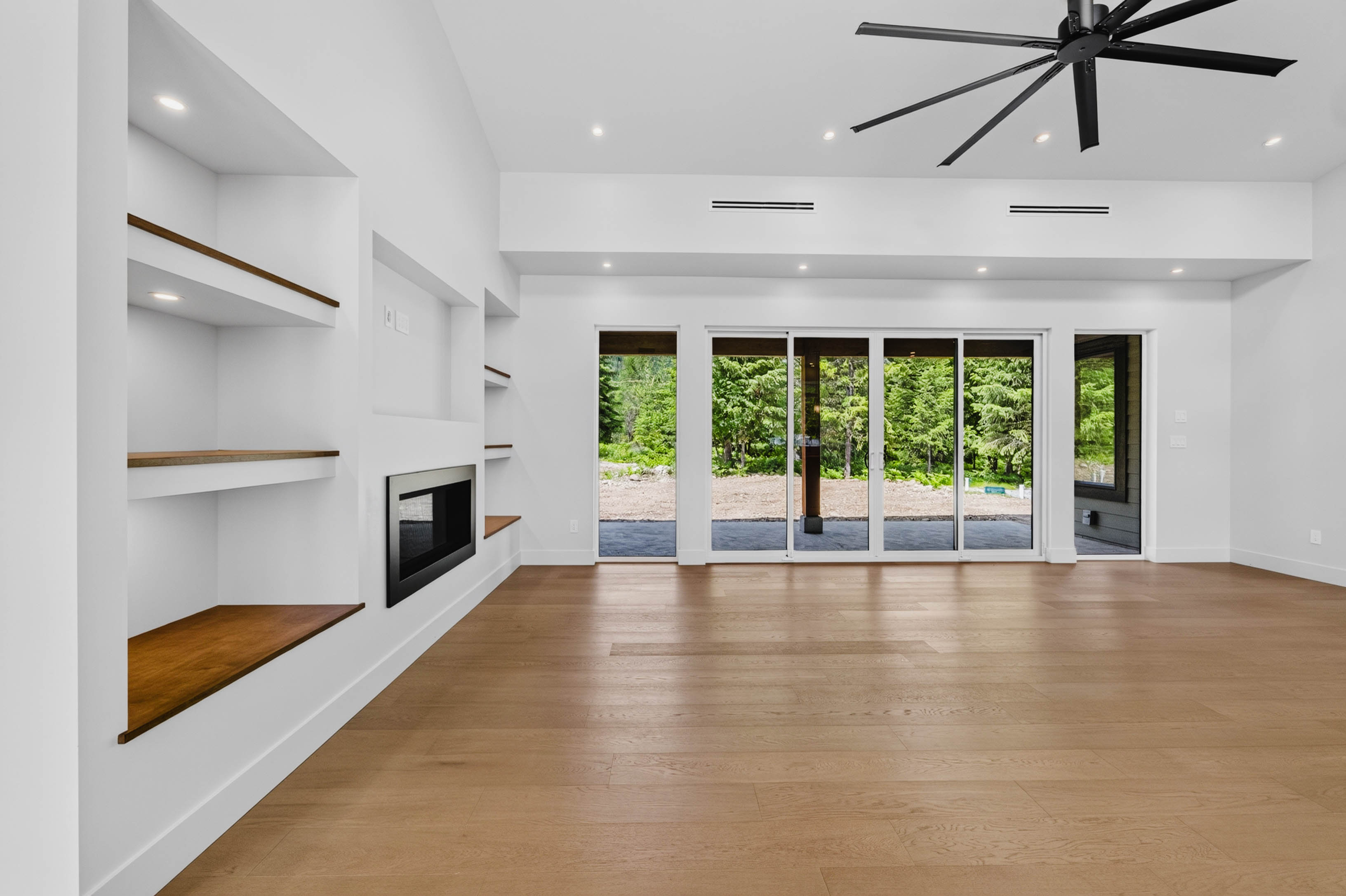 Open-concept living room at 7769 Holt Road with vaulted ceiling, gas fireplace, built-ins, and patio doors