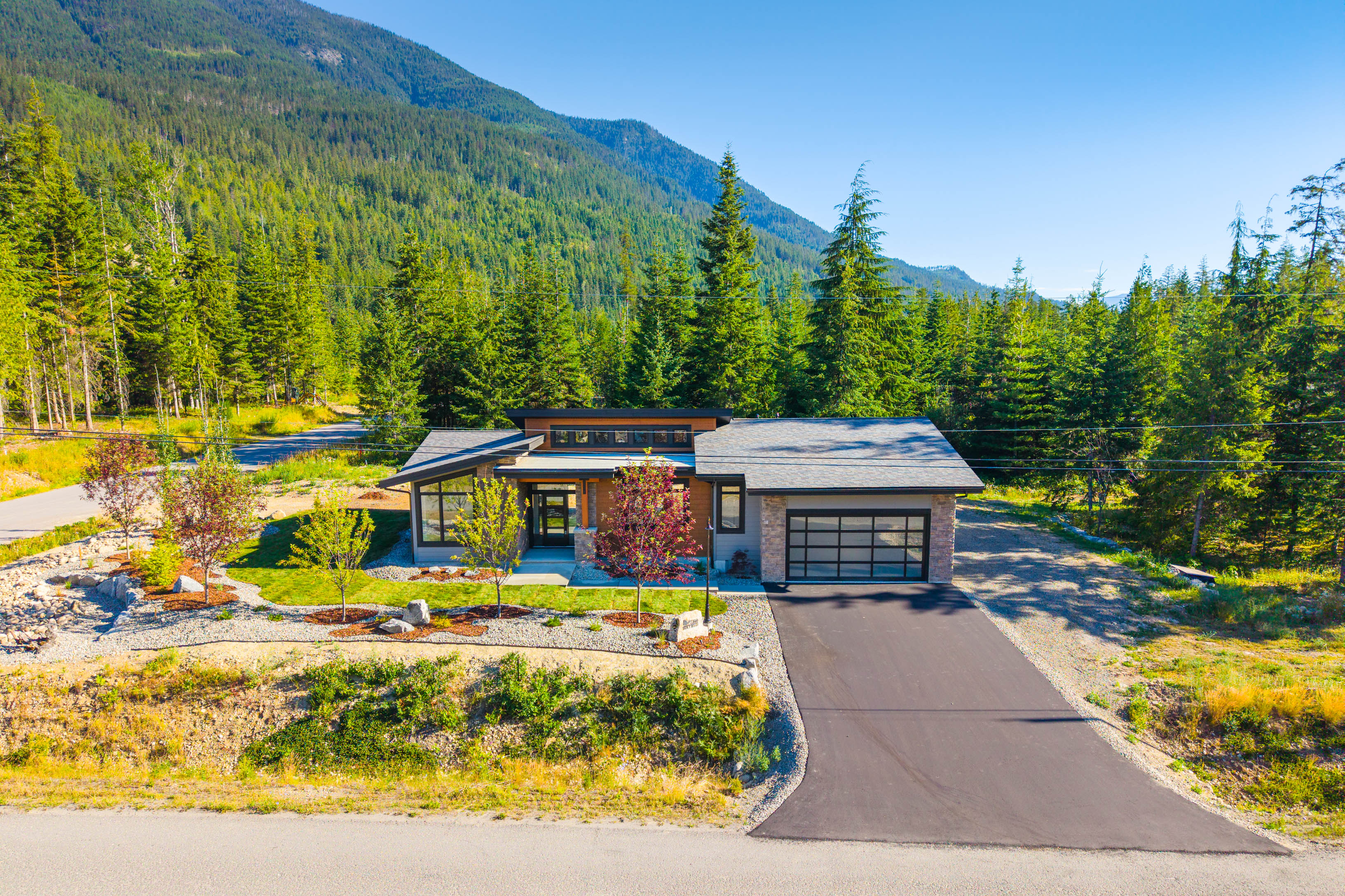 Updated aerial front view of the brand-new rancher at 7769 Holt Road in Balfour BC, surrounded by forest and mountains