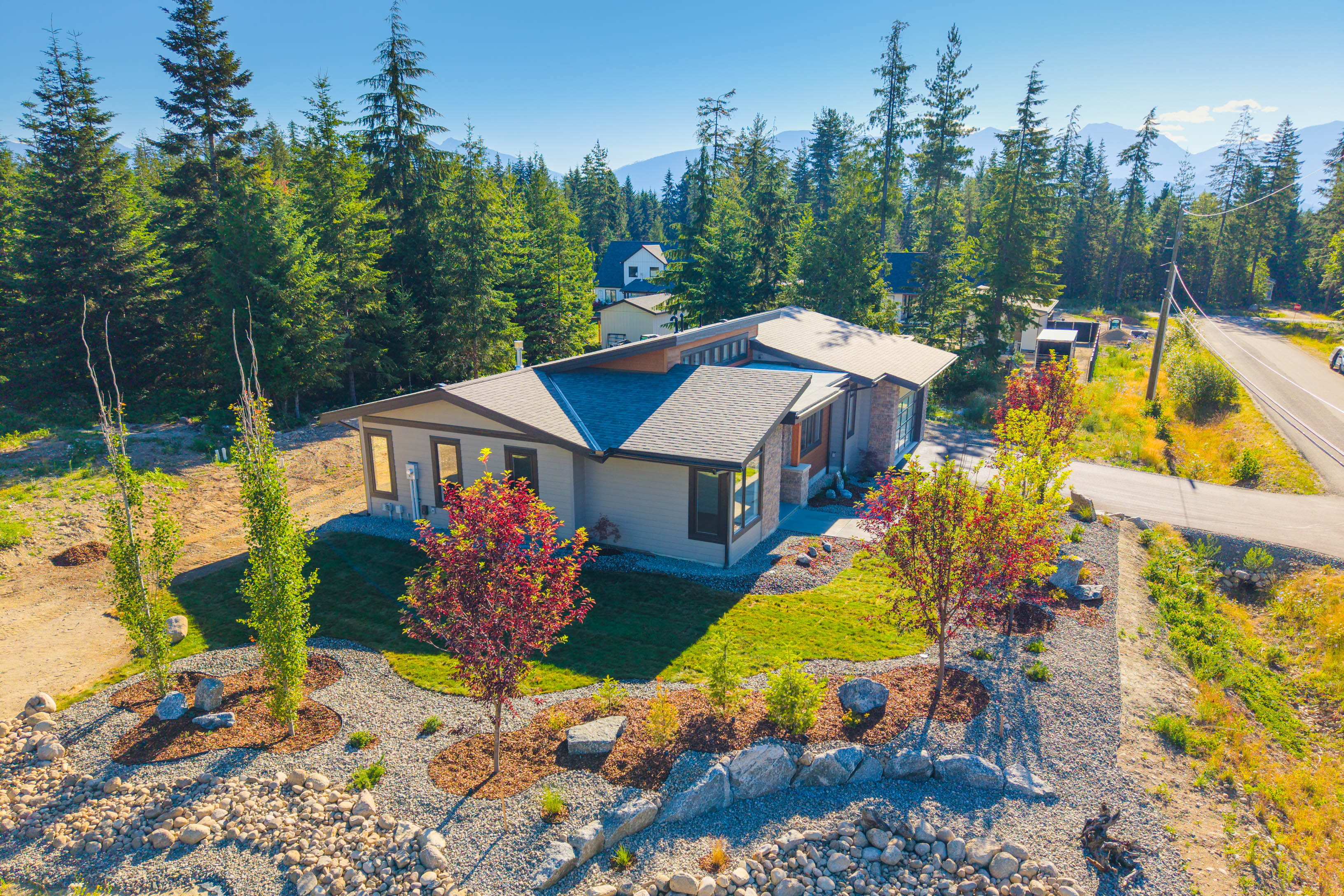 Updated aerial view of 7769 Holt Road showing the landscaped corner lot, surrounding forest, and mountain setting