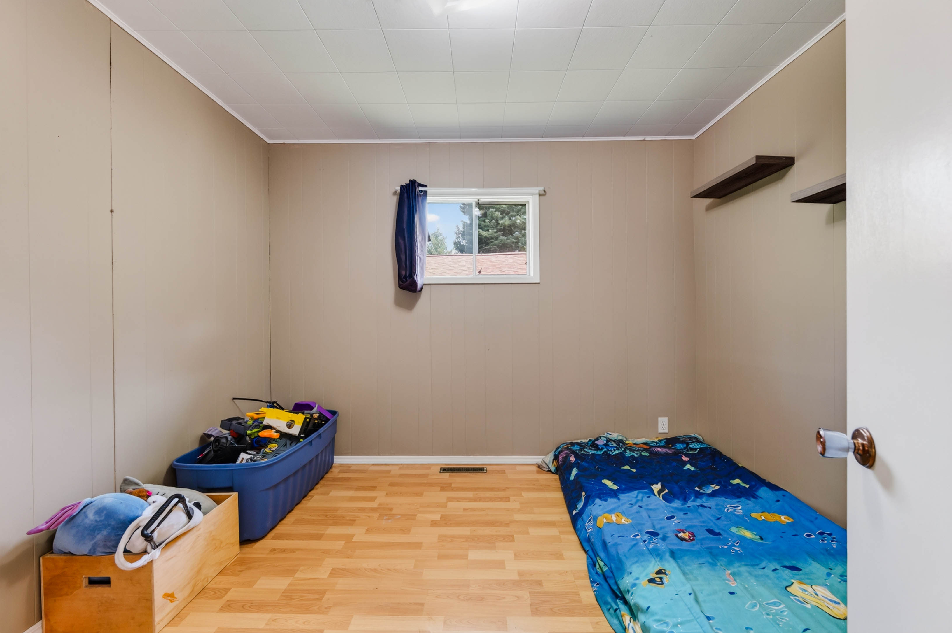 Third bedroom with wood-look flooring, wall shelves and natural light