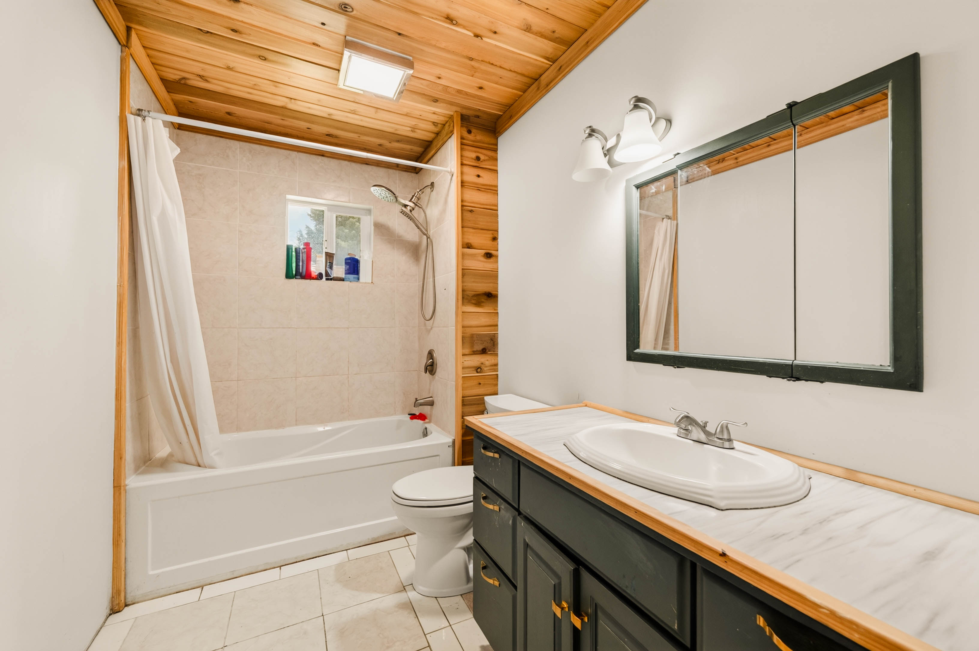Main bathroom with dark vanity, tiled tub surround and warm wood ceiling