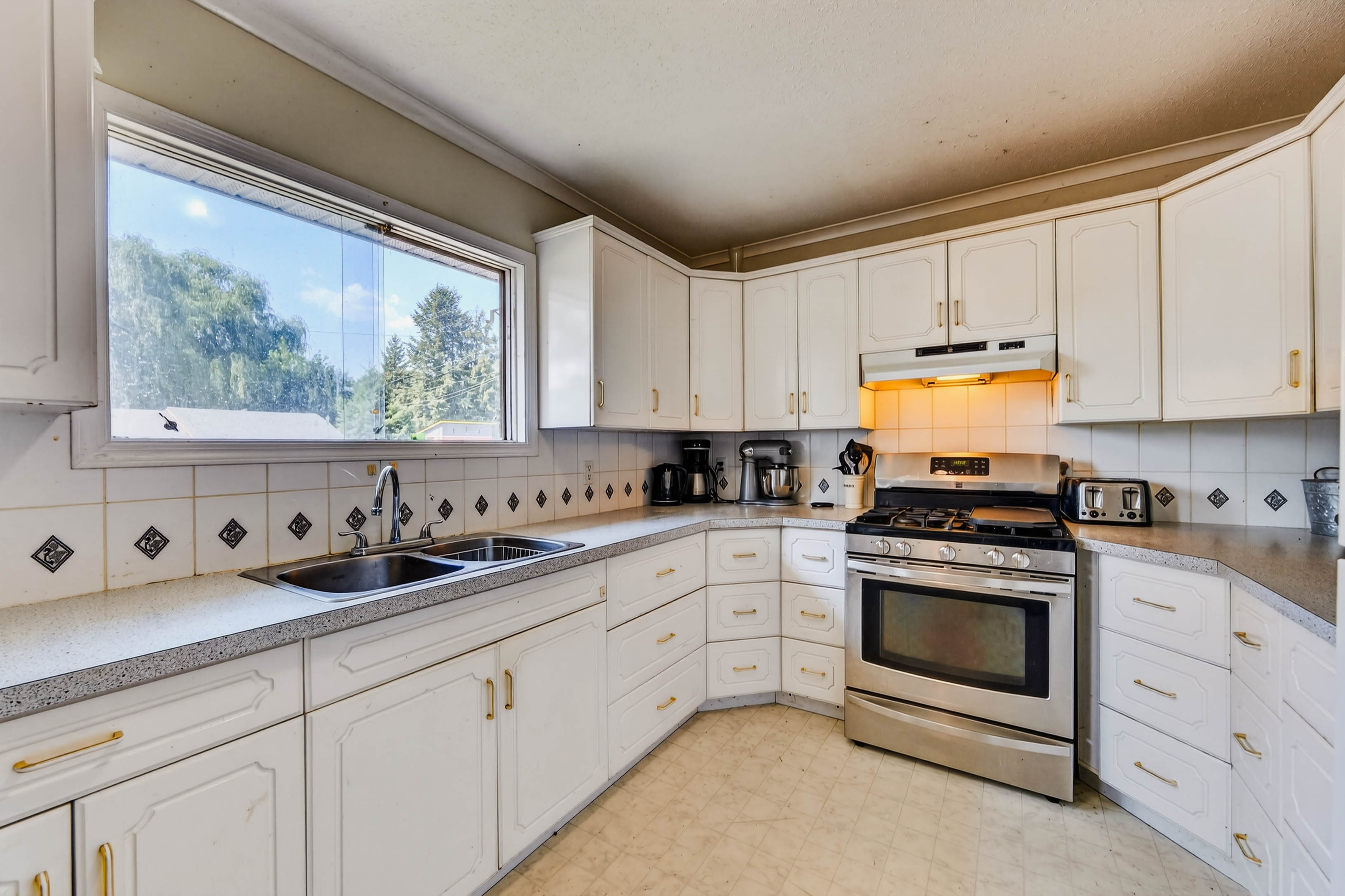 Bright kitchen with white cabinetry, a window over the sink and stainless steel range