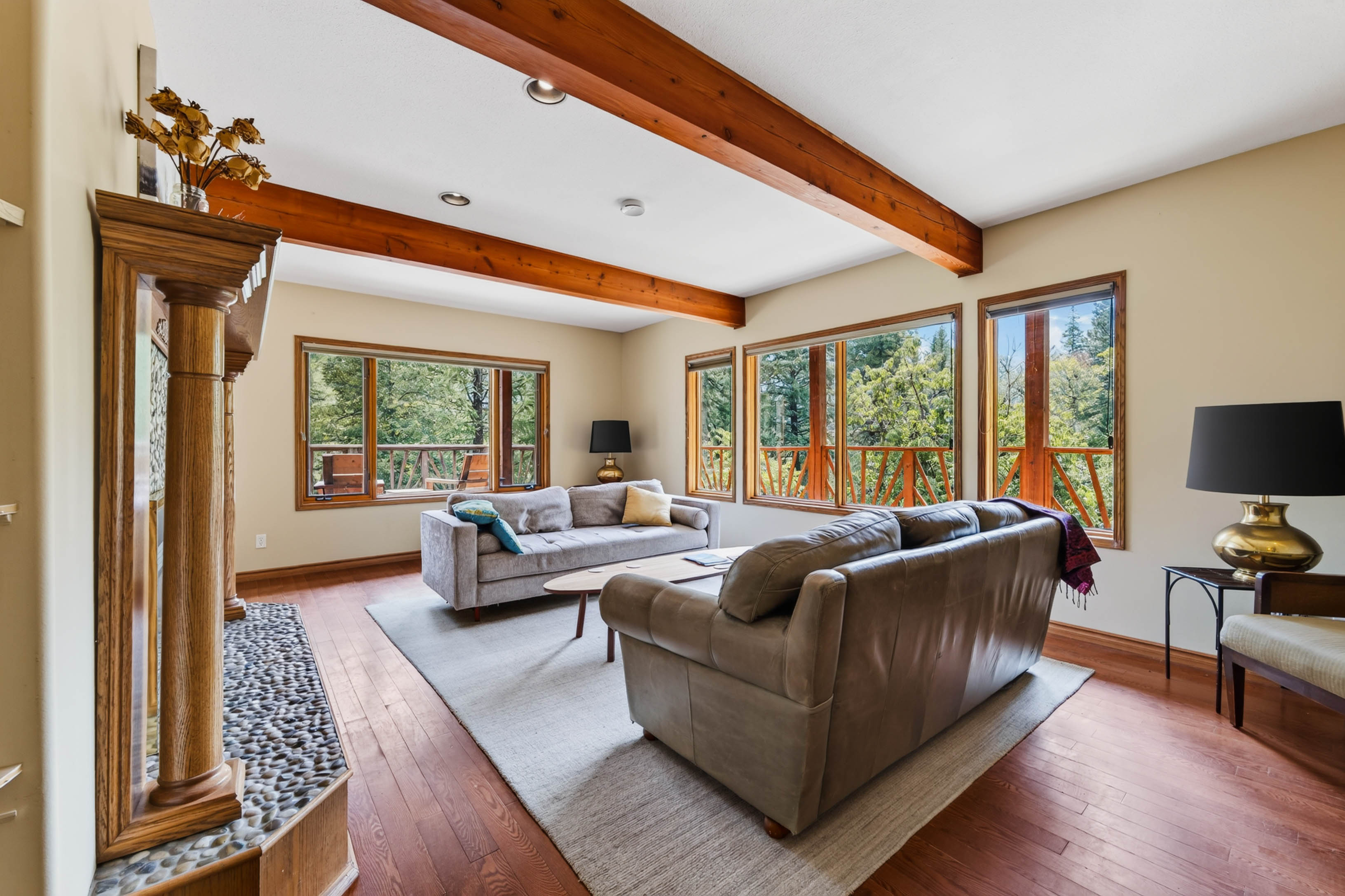 Bright living room at 3360 Little Slocan South Road with exposed wood beams, large windows and views into the surrounding trees.