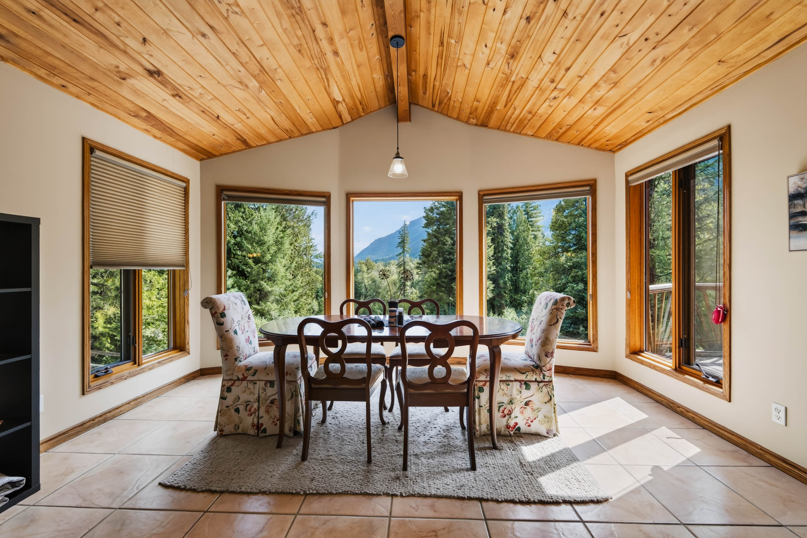 Bright dining area at 3360 Little Slocan South Road with vaulted wood ceiling, large windows and views toward the surrounding landscape.