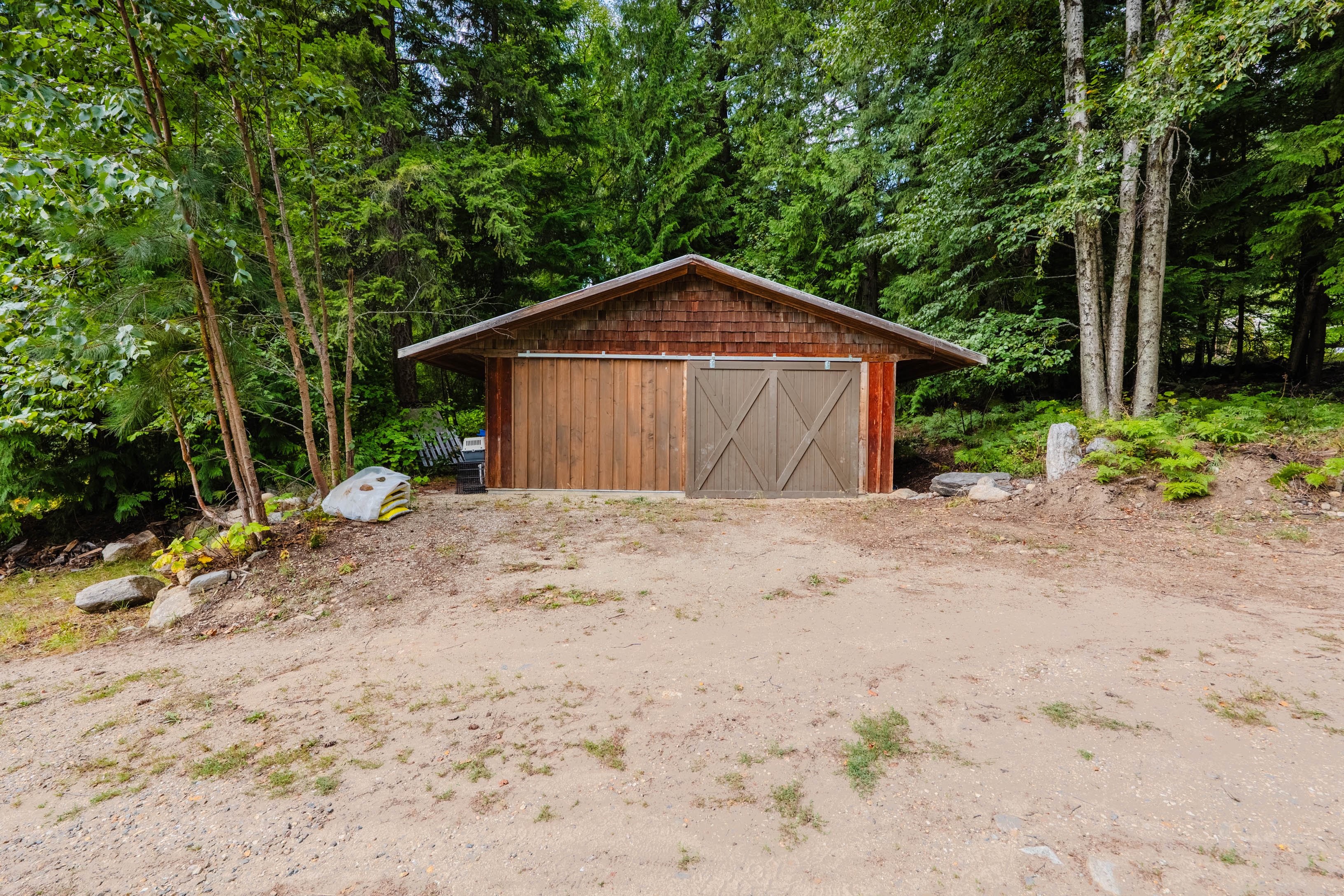 Wood outbuilding at 3360 Little Slocan South Road set within the forested acreage.