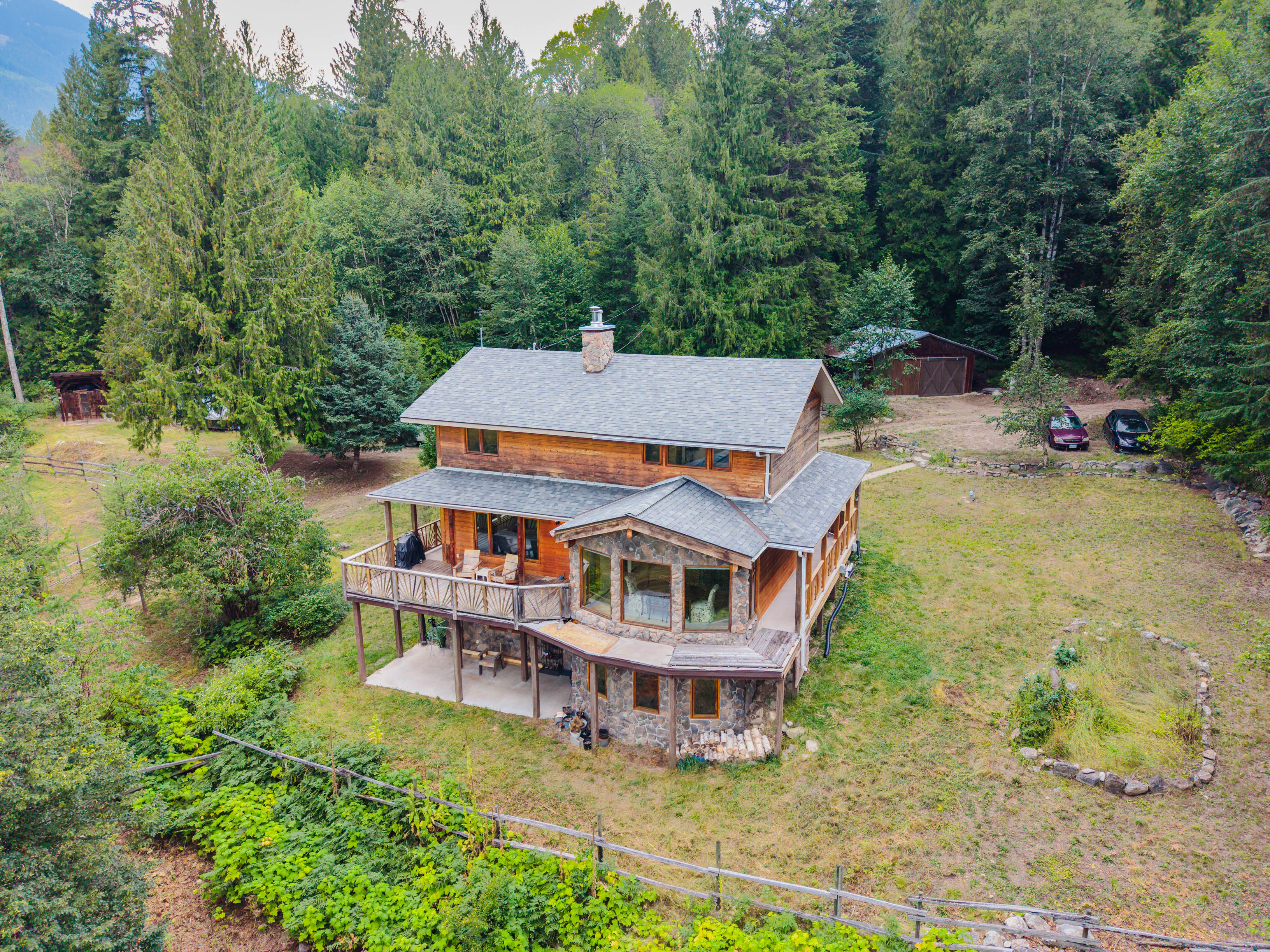 Exterior view of the home at 3360 Little Slocan South Road in Passmore, BC, surrounded by mature trees and open yard space.