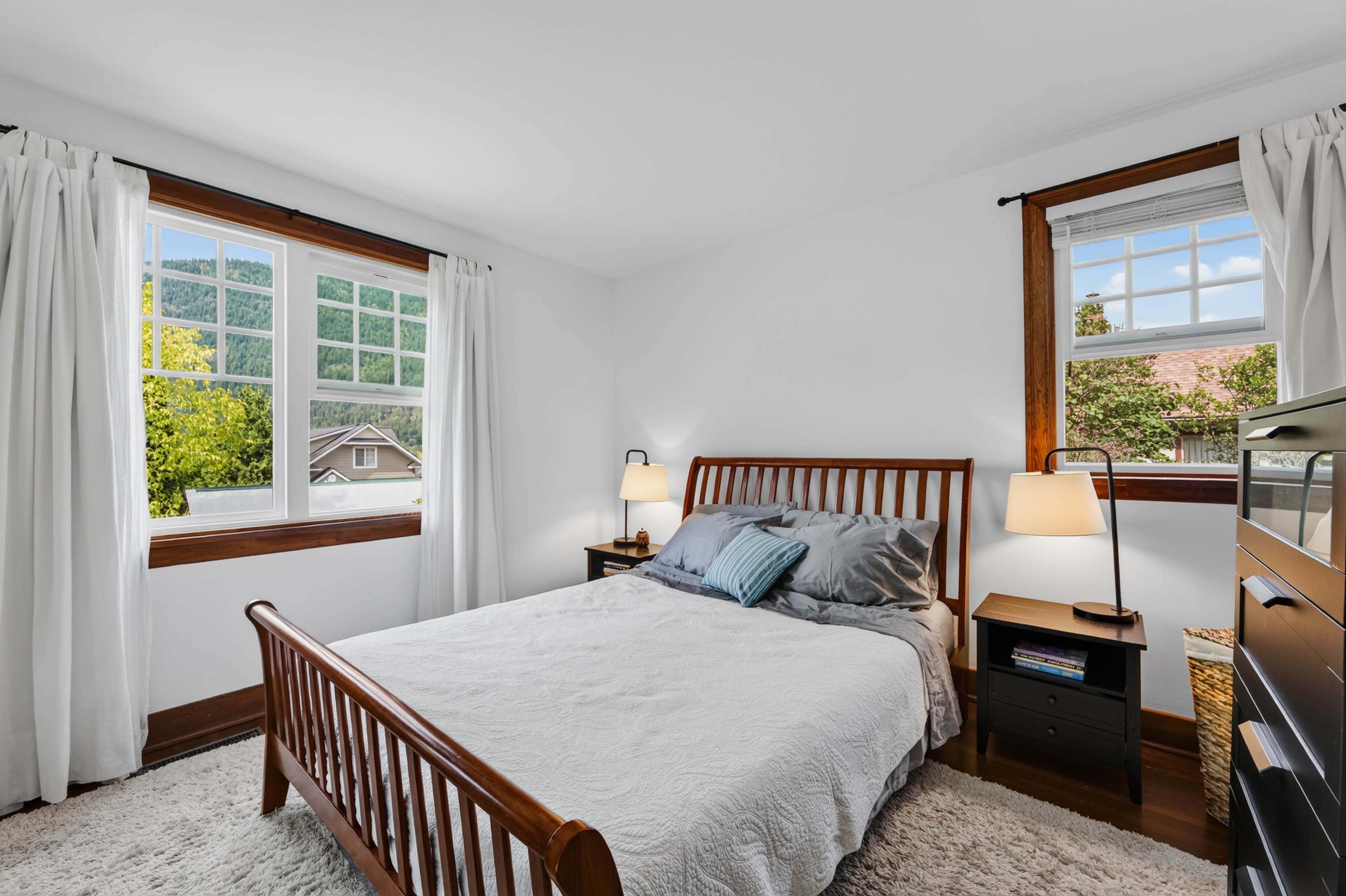 Bedroom with two wood-trimmed windows and a wooden bed frame