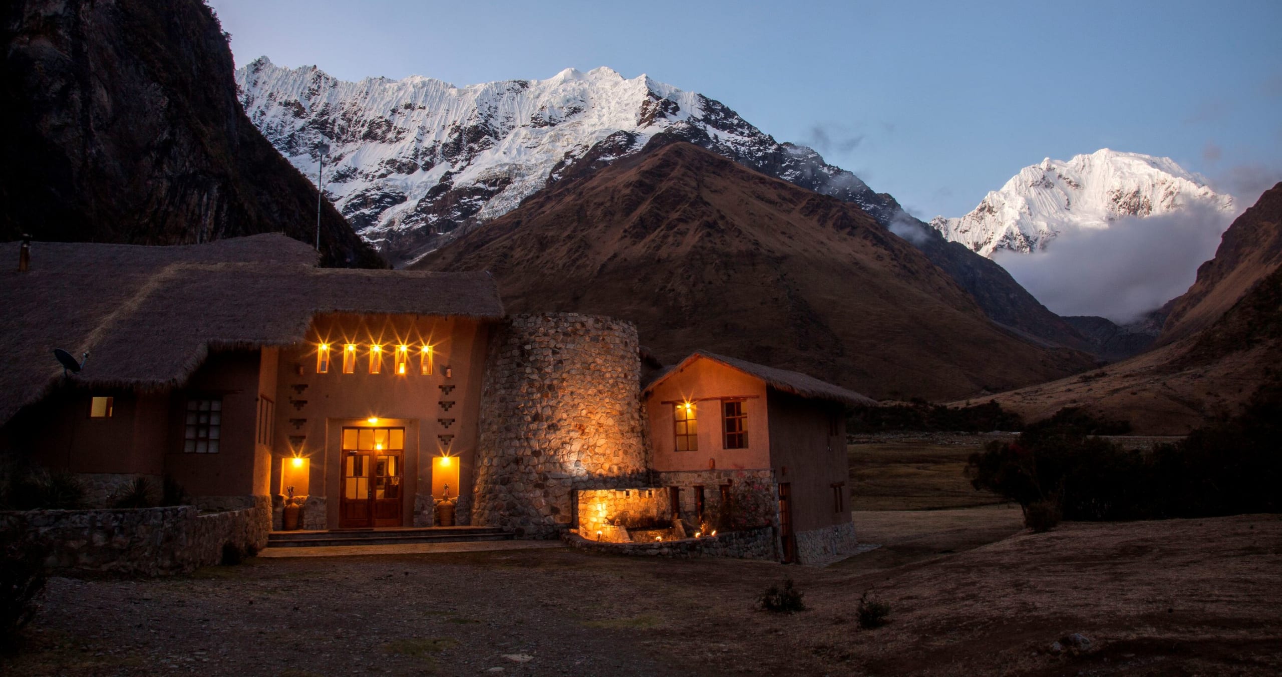 Salkantay Lodge glowing at dusk beneath the snow-capped Salkantay massif