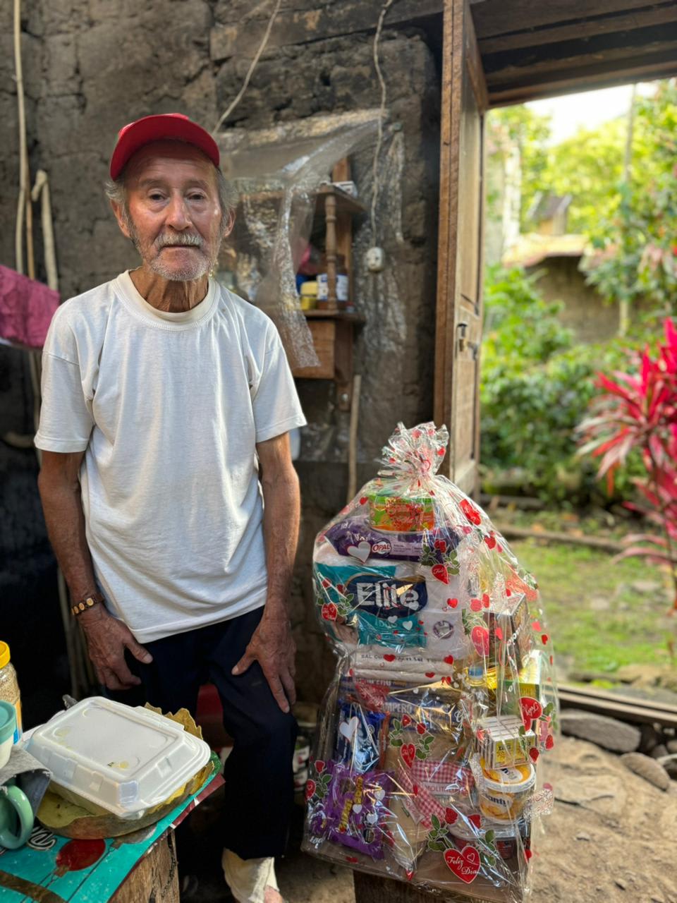 An elder standing next to a wrapped gift basket at his home