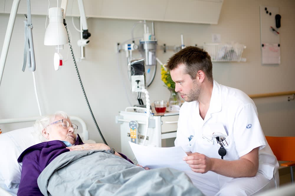 Bild av läkare som sitter och lyssnar på sin sängliggandes patient.