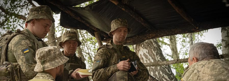 Бійці на нараді під маскувальною сіткою біля польового стола зі засобами зв'язку
