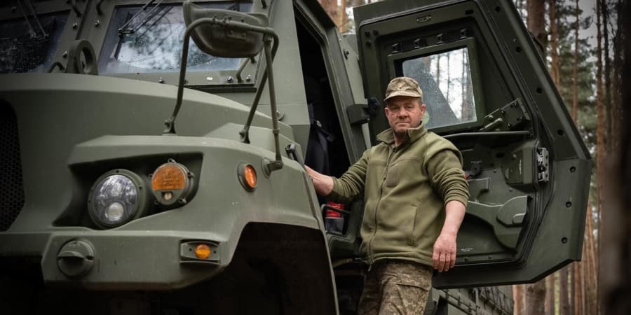 Військовий біля відчинених дверей бронеавтомобіля в лісі