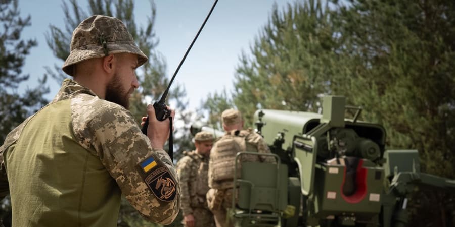 Боєць з радіостанцією та шевроном України на позиції біля гаубиці