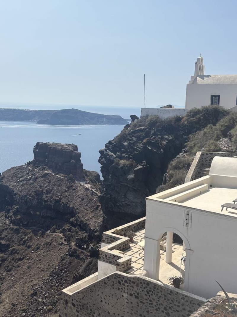 A resort pool carved into the Oia caldera cliff — white cave houses cascading below