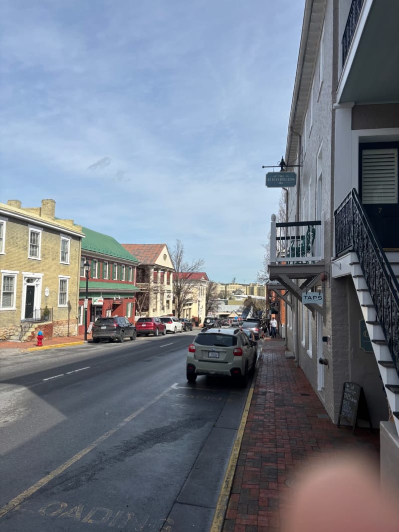 # Alt Text
A charming historic street lined with colorful brick buildings, parked cars, and storefronts under a clear blue sky.