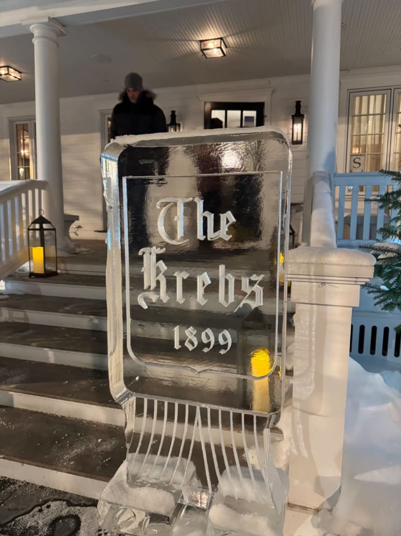 An ice sculpture reads "The Brechs 1899" on a snowy porch with white columns and lanterns.