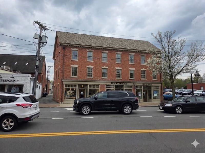 A historic brick building with ground-floor shops and apartments above, located on a main street with parked cars and utility poles.