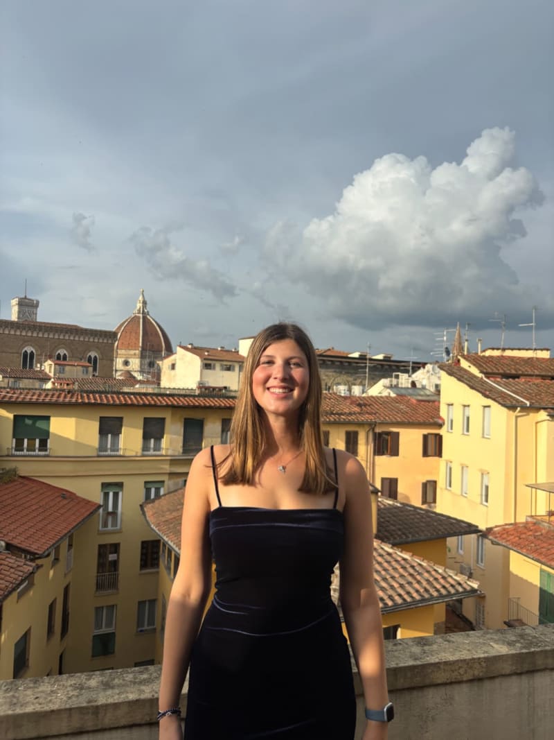 Woman in black dress smiling on a rooftop terrace overlooking Florence's historic architecture and the Duomo.