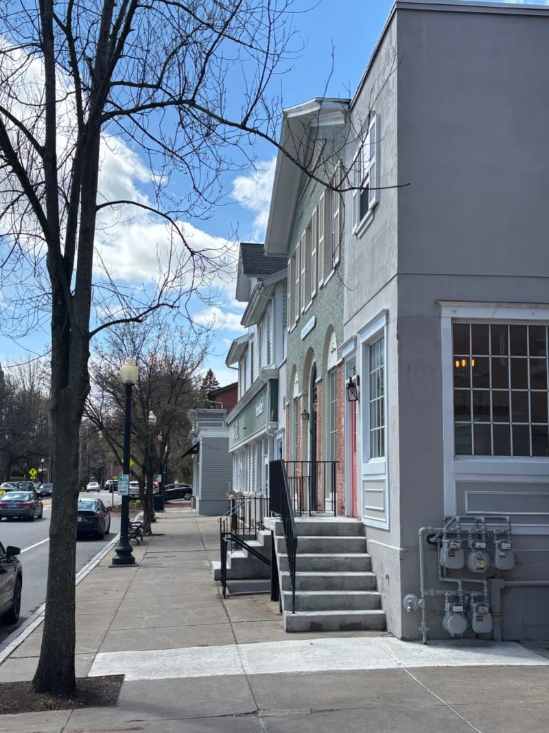 A row of historic townhouses lines a residential street with bare trees and clear blue sky.