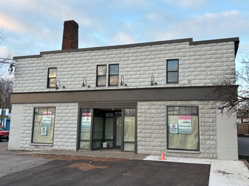 # Alt Text
Two-story brick commercial building with white painted stone facade, large storefront windows, and "Available" signs indicating vacant retail space.