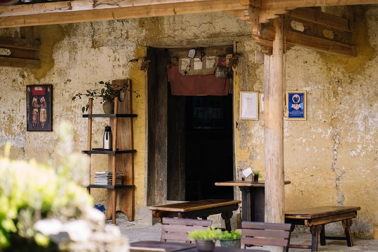 Hiên trước quán Cafe Cực Bắc với kệ gỗ, bàn ghế và cửa vào nhà cổ