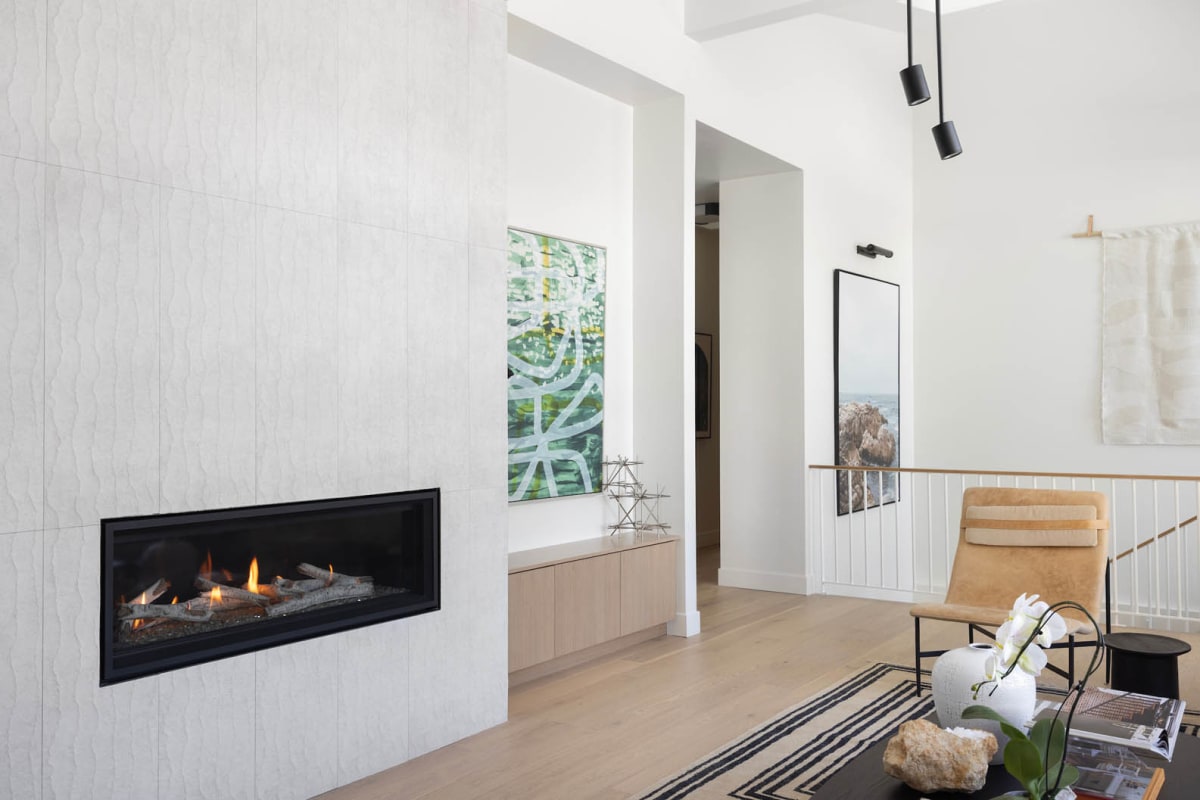 Living room with a linear gas fireplace set into a white textured tile wall, beside a leather sling chair and striped rug
