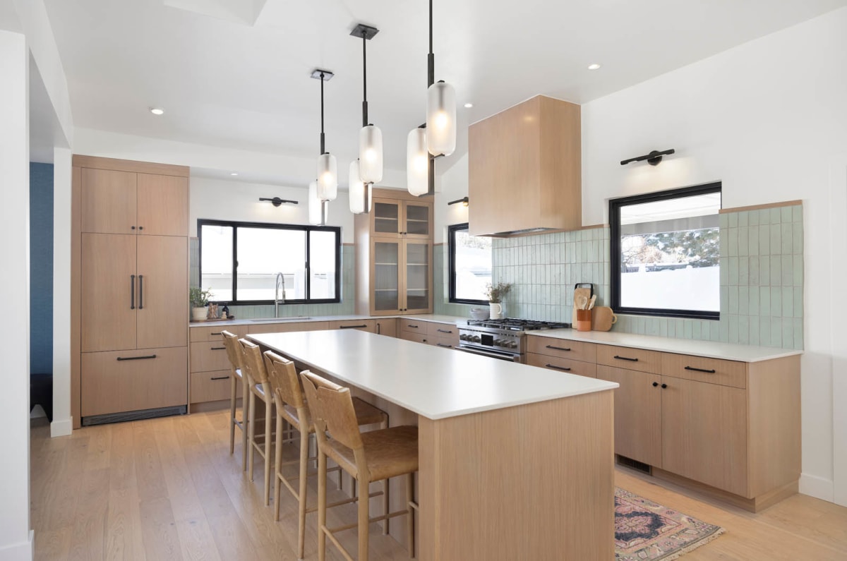 White oak kitchen with a long island, glass globe pendants, green tile backsplash and black-framed windows
