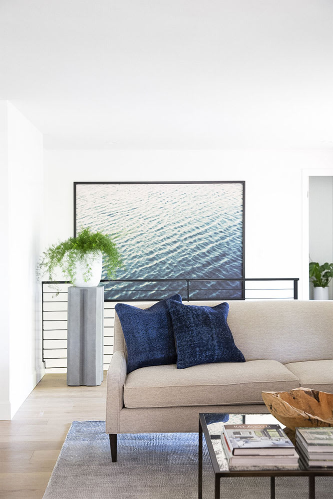 Cream sofa with indigo pillows below a large framed photograph of rippling water, beside a black stair railing